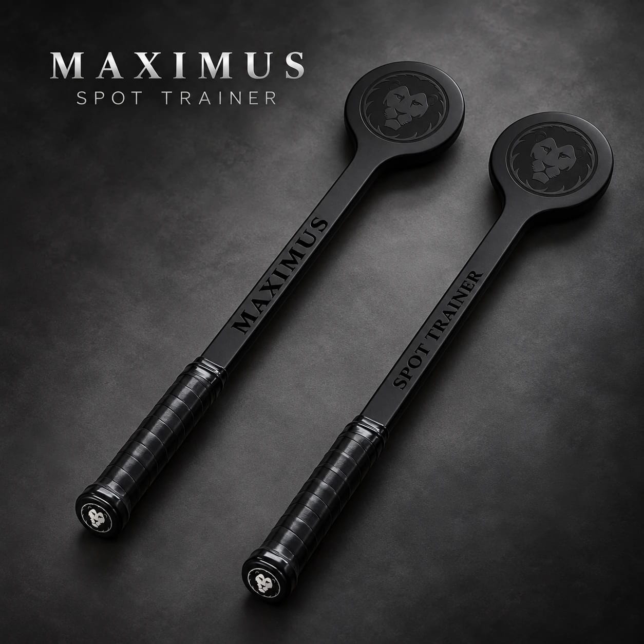 Two MAXIMUS Spot Trainers laid at an angle on a dark surface, MAXIMUS engraved along one shaft and SPOT TRAINER along the other, with the lion roundel on each contact head